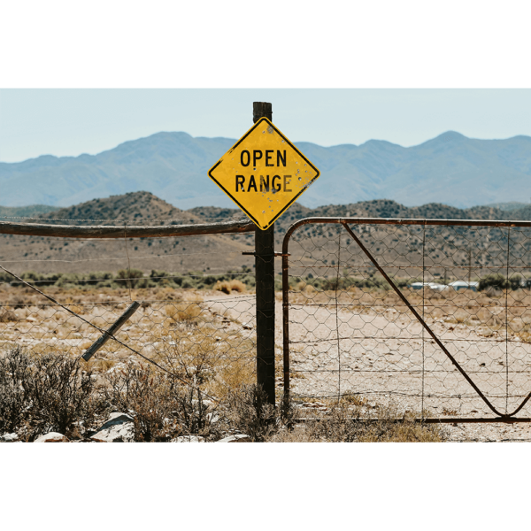 An Open Range Warning Sign on a fence post in a desert.