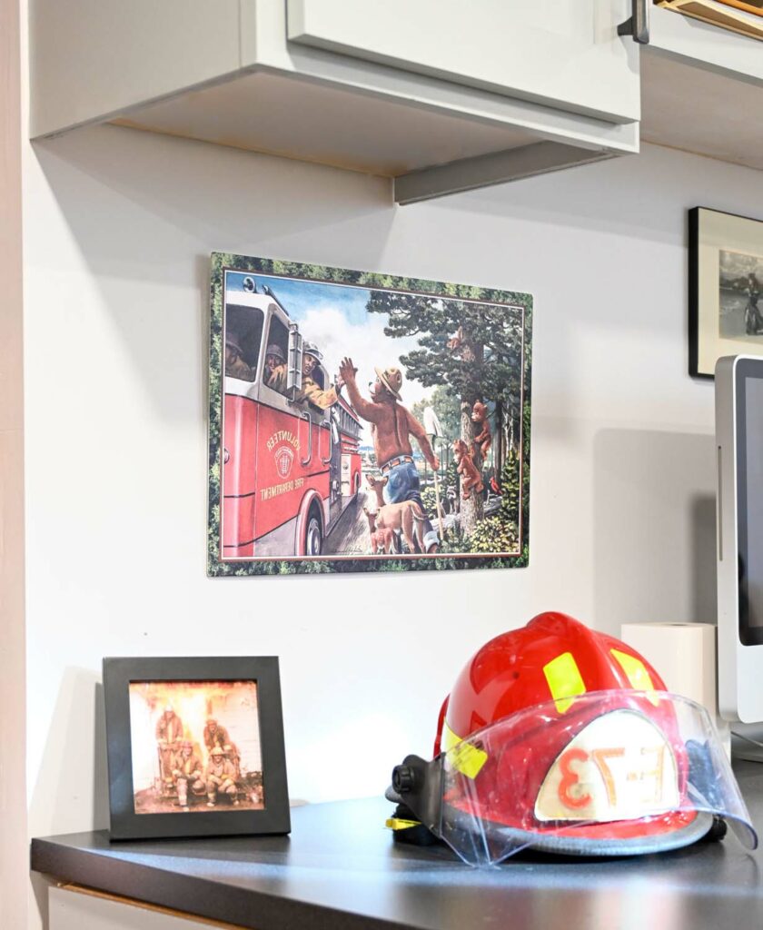 Wall art of smokey bear giving a high five to a firefighter, hung up in front of a firefighter helmet