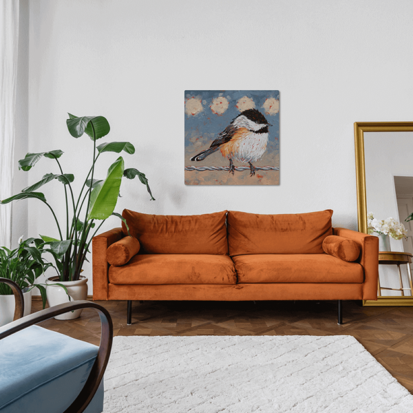An aluminum print of Chickadee on a Wire hung up above a couch.